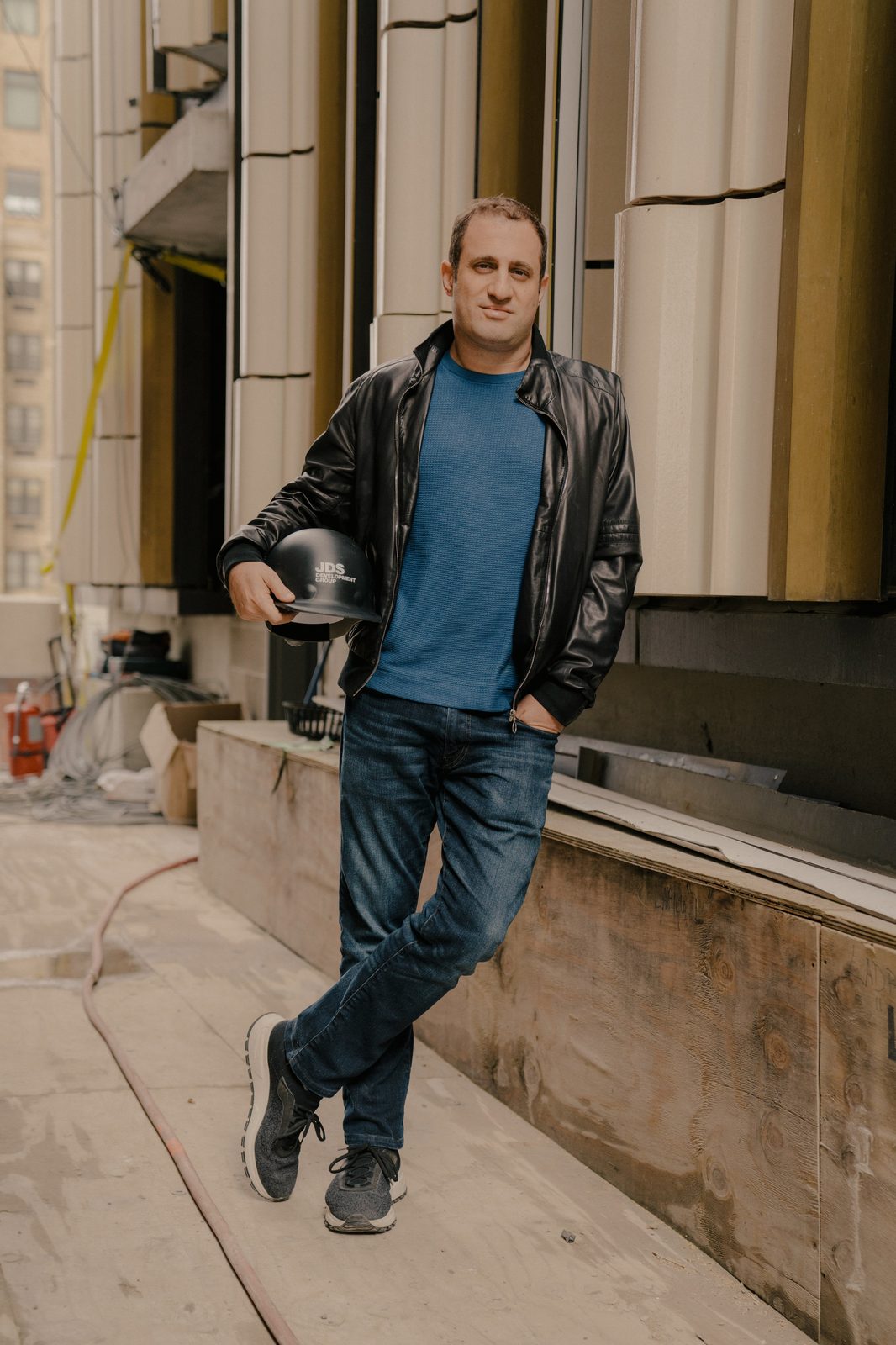 Michael Stern stands against a construction hoarding holding a JDS hard hat.